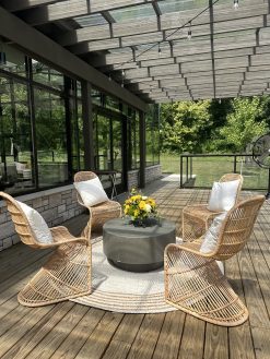 Four rattan light colored cruved chairs around a gray coffee table on a round rug