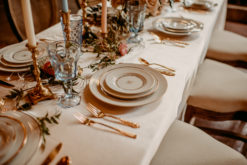 Romantic table setting for wedding reception with gold and white plates, vintage gold flatware, blue goblets and florals