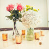 Vases with bright florals in the center of a table surrounded by gold votives