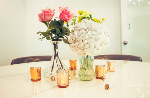 Vases with bright florals in the center of a table surrounded by gold votives