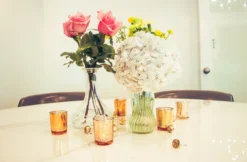 Vases with bright florals in the center of a table surrounded by gold votives