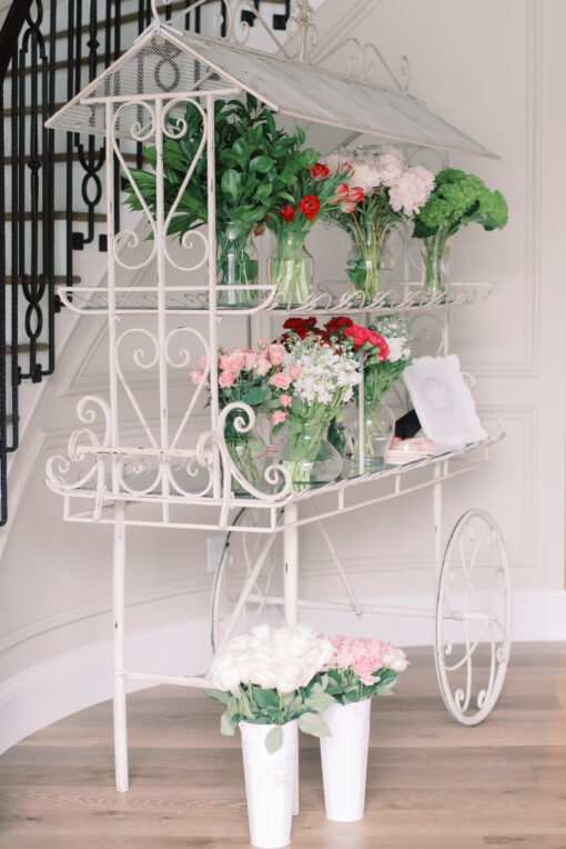 Elegant white display cart with two tiers holding flowers.