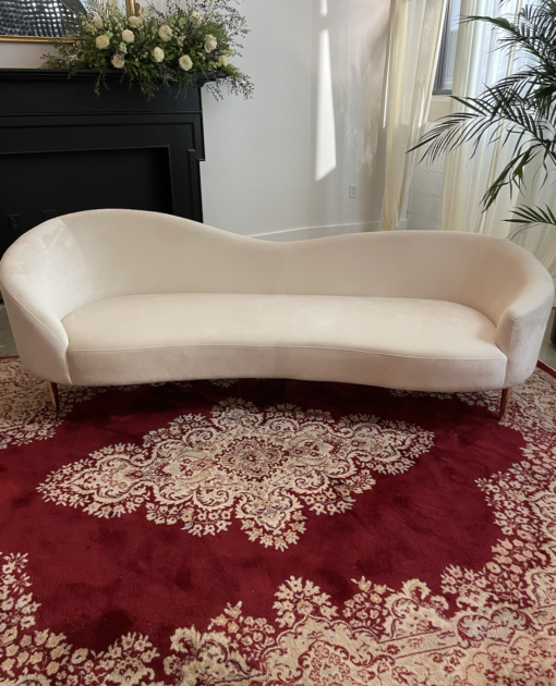 White velvet curved sofa with a bold red rug and elegant design pattern.