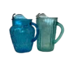 Two vintage pitchers next to each other. One is more rounded and primary blue. The other is skinny and slightly teal.