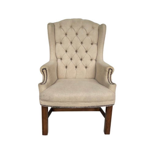 Tan high back wing chair with button tufting and nail head trim on arms. Dark wood legs.