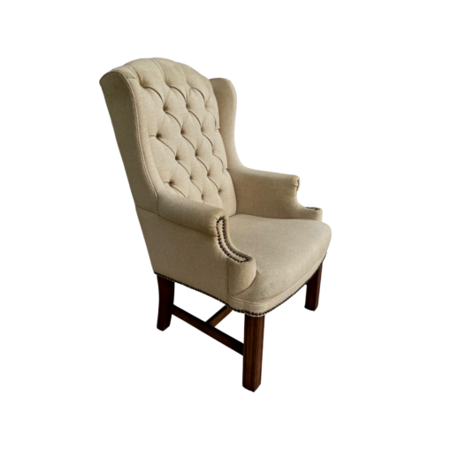 Tan high back wing chair with button tufting and nail head trim on arms. Dark wood legs. Side angle