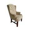 Tan high back wing chair with button tufting and nail head trim on arms. Dark wood legs. Side angle