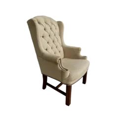 Tan high back wing chair with button tufting and nail head trim on arms. Dark wood legs. Side angle