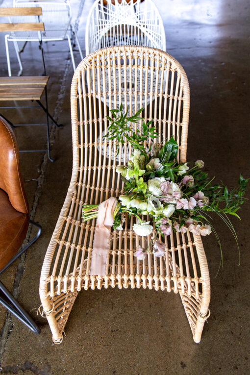 Light brown rattan chair with florals on a polished concrete floor.