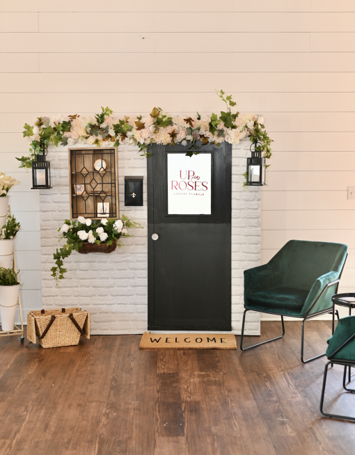 Vendor created backdrop with a foot door, florals, welcome mat and dark green velvet chairs.