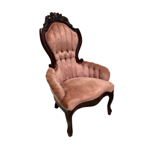 Victorian arm chair with pink velet, channel tufted back, dark wood ornate trim and rolled arms.