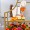 Close up on upper portion of gold shelf. Wine glass with bright orange welcome drink, sliced fruit and florals