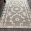 Neutral rug with tan backing and cream tufted geometric symmetrical pattern.