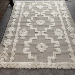 Neutral rug with tan backing and cream tufted geometric symmetrical pattern.