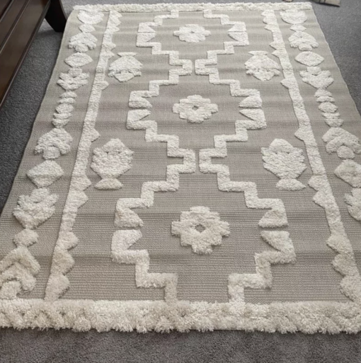 Neutral rug with tan backing and cream tufted geometric symmetrical pattern.