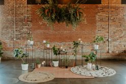 A modern event vignette with a brick wall, layered rugs, potted plants, and contemporary lounge furniture, creating an inviting atmosphere.