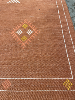 Close up of the white line border on the rug. Orange and yellow diamonds around the edge.