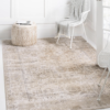 Rug placed on a white floor with white walls and white chairs with a neutral pouf