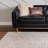 Rug on a brown wooden floor with black sofa and white walls