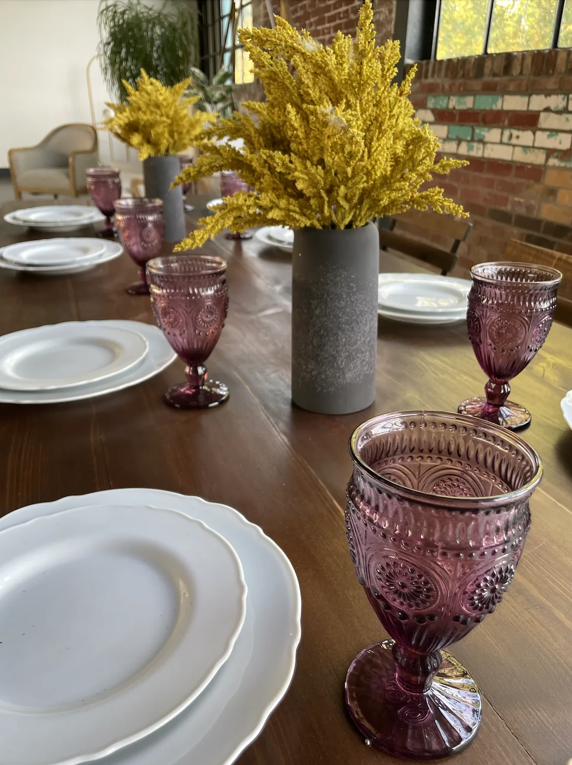 Table top with white plates, plum goblets and goldenrod florals WEBP Wooden farmtable with white plates, plum matching goblets and goldenrod plant in a gray ceramic vase