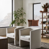 2 natural linen barrel chairs in a lounge with plant and bookshelf in background. Rug and coffee table corner in forground.