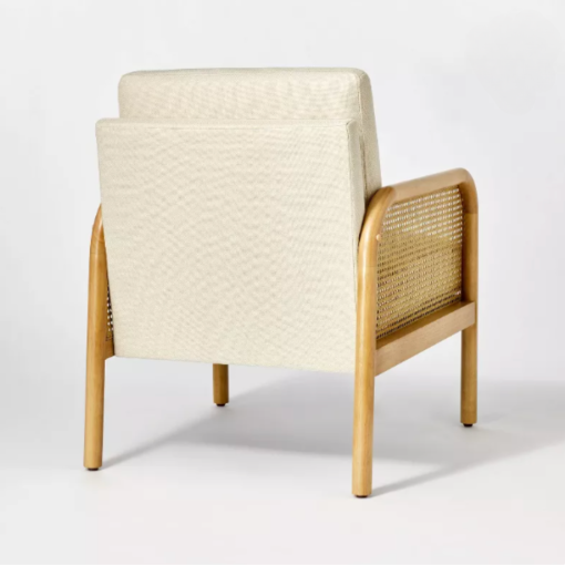 Back angle view of chair. Back is cream upholstery with cushion rising above. Side of cane based arms.