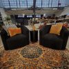 Two fuzzy black swivel chairs in a seated area with side table and a vintage orange rug. In an industrial space with high windows.