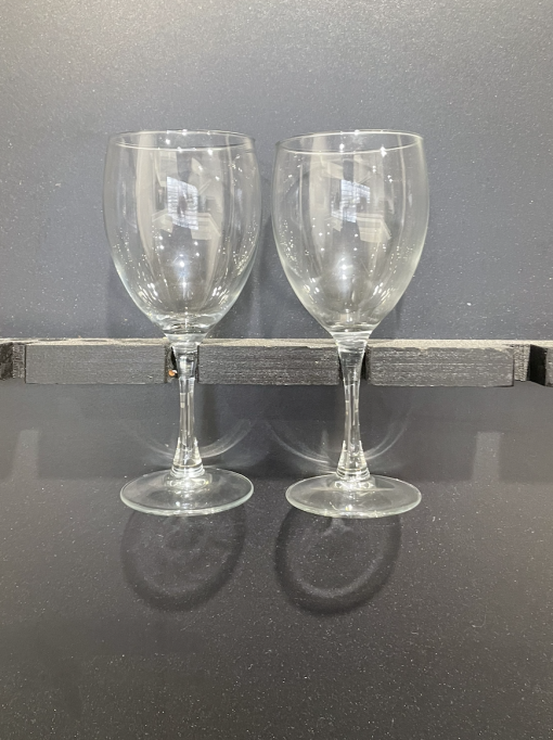 Two classic wine glasses held by the stem on a rack with a black background.