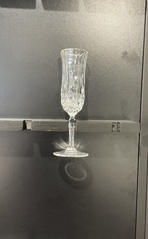 One crystal etched glass champagne flute held by the stem. Black background.