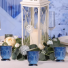 Center piece with white lantern, greenery surrounding, and blue glass votives.