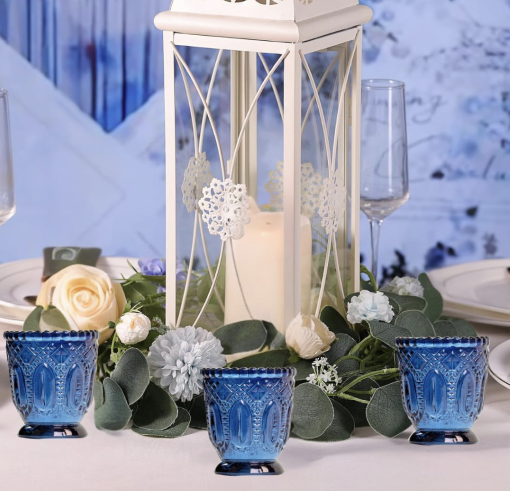 Center piece with white lantern, greenery surrounding, and blue glass votives.