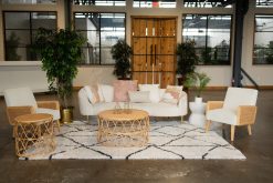 Modern boho lounge rental for a birthday party in a downtown Indianapolis warehouse venue, featuring a curved cream velvet sofa, rattan accent chairs, and a geometric rug.