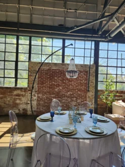 Gala Chandelier freestanding black chandelier over round table with ghost chairs and blue glassware at brick venue