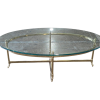 Travis Coffee Table for rent at Violet Vintage Indianapolis: A mid-century modern oval coffee table with a clear glass top, a gold-finished brass metal frame, and slim legs with decorative feet.