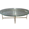 Travis Coffee Table for rent at Violet Vintage Indianapolis: A mid-century modern oval coffee table with a clear glass top, a gold-finished brass metal frame, and slim legs with decorative feet.
