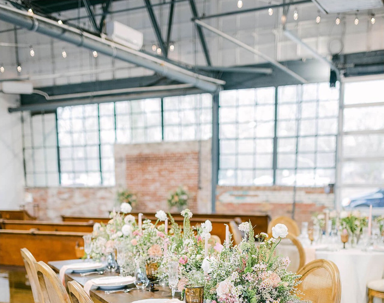 Dining tables and chairs arranged inside The VV Showroom with exposed brick and factory windows