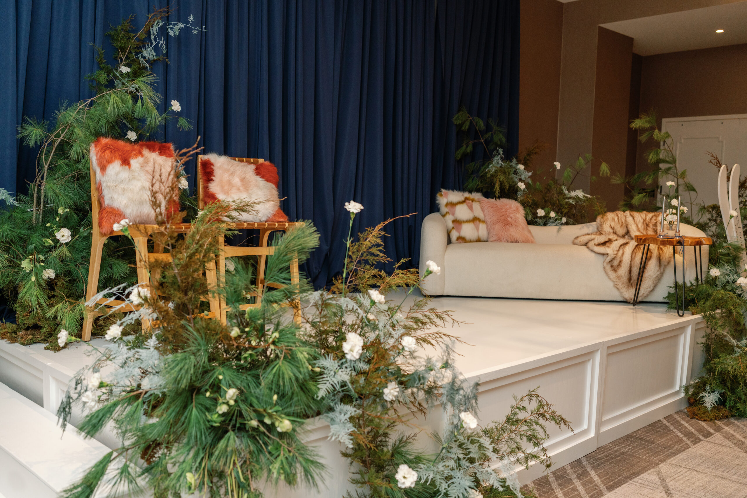 Furnished conversation stage at InterContinental Indianapolis with two woven chairs, a cream Kanissu Sofa, greenery, and a wood Tress Side Table
