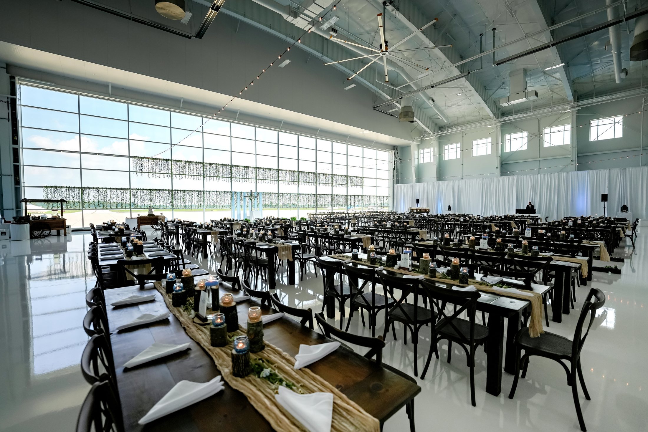 Clear view of Kingston Farmtables and Dark Resin Vineyard Cross Back Chairs styled for a wedding reception at Beck's Hangar in Zionsville.