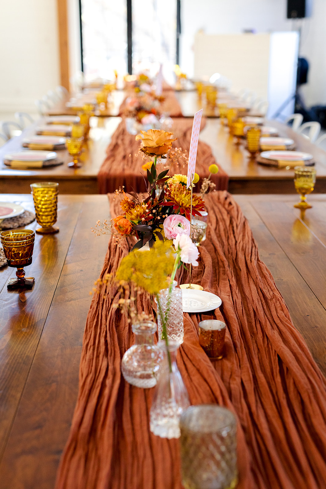 Amber goblets and a rust runner on a wood wedding reception table at The Wilds
