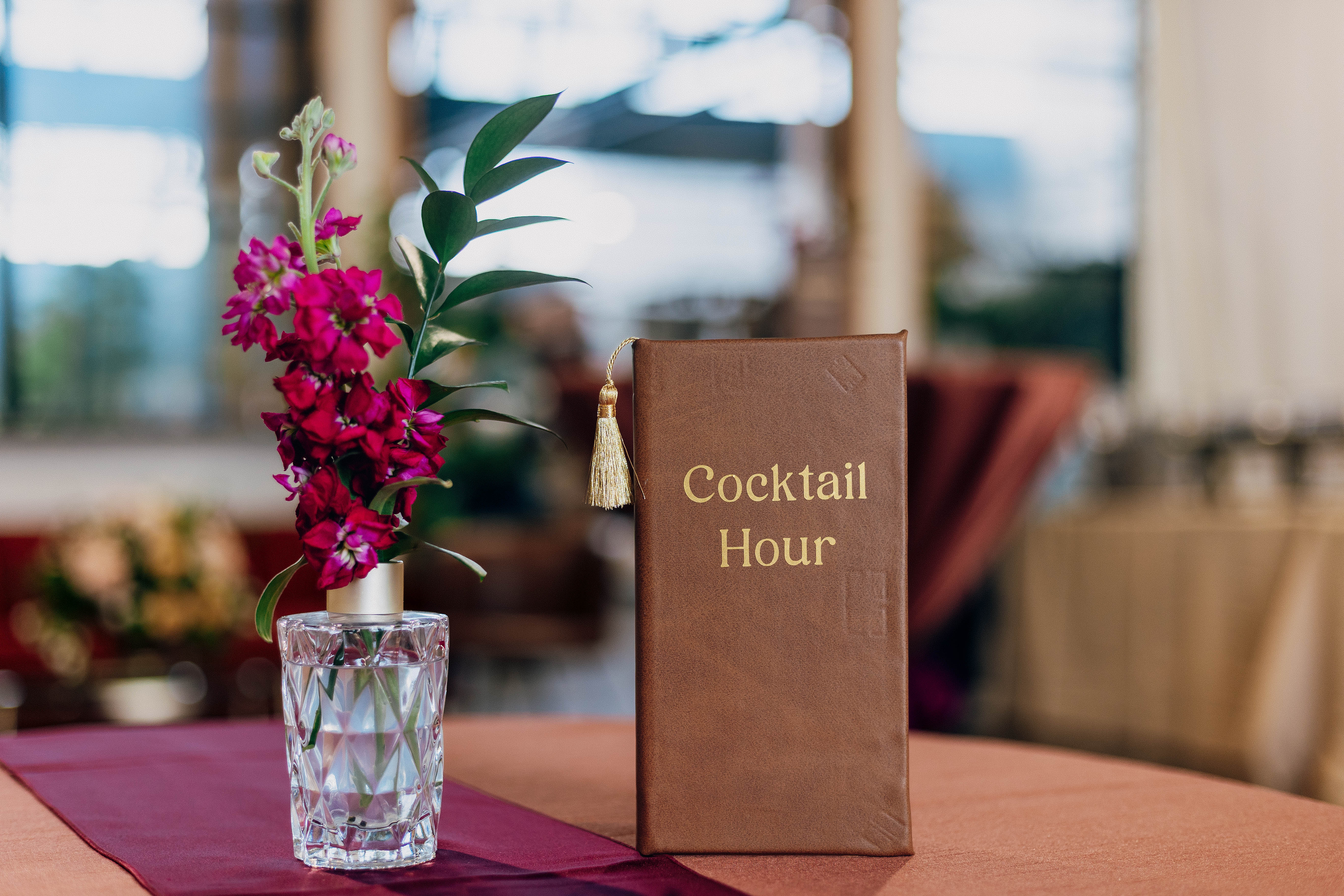 Cocktail Hour card beside a burgundy runner and floral detail at Folake and Aloy's VV Showroom wedding