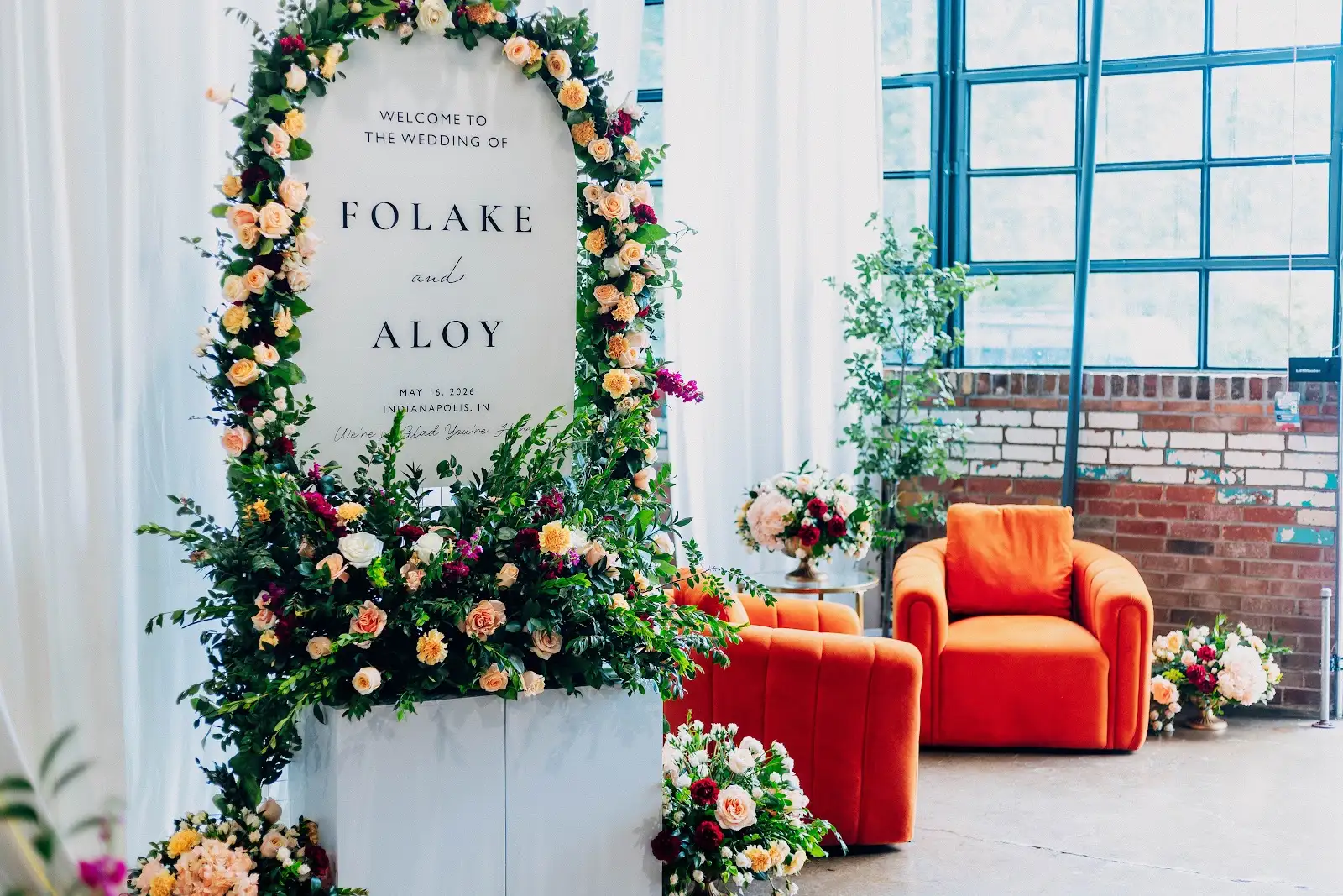 Folake and Aloy wedding welcome sign with florals and two orange Tangerine Twist Chairs at VV Showroom