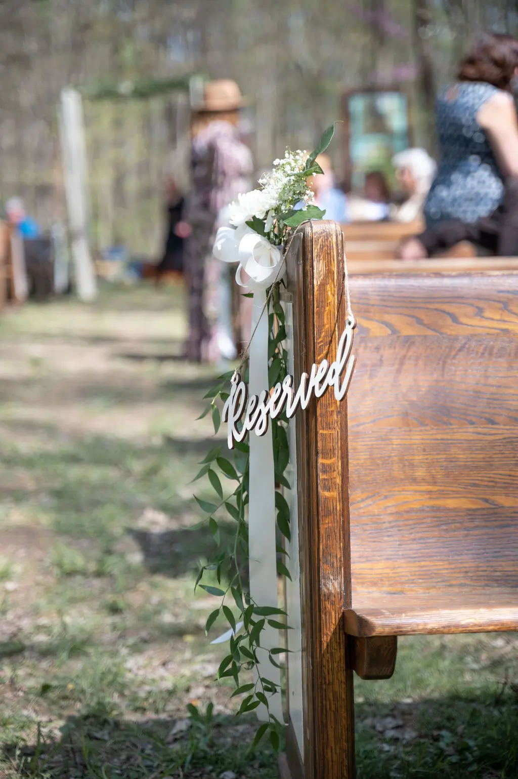 Reserved sign, greenery, and ribbon on a vintage wood church pew at an outdoor wedding ceremony
