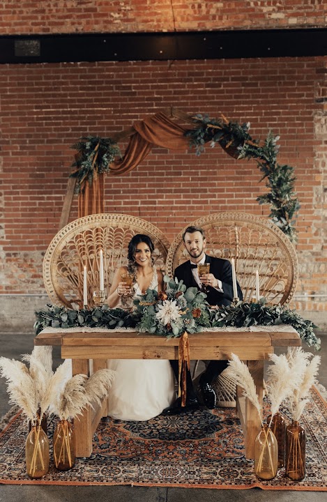 Sierra and Austin seated at their Daniela Peacock Chair sweetheart setting with the Genevieve Geometric Arch and Savannah Rug at INDUSTRY in Indianapolis