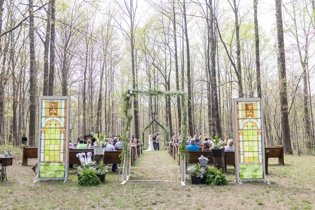 Vintage church pew rows defining a wooded outdoor wedding ceremony