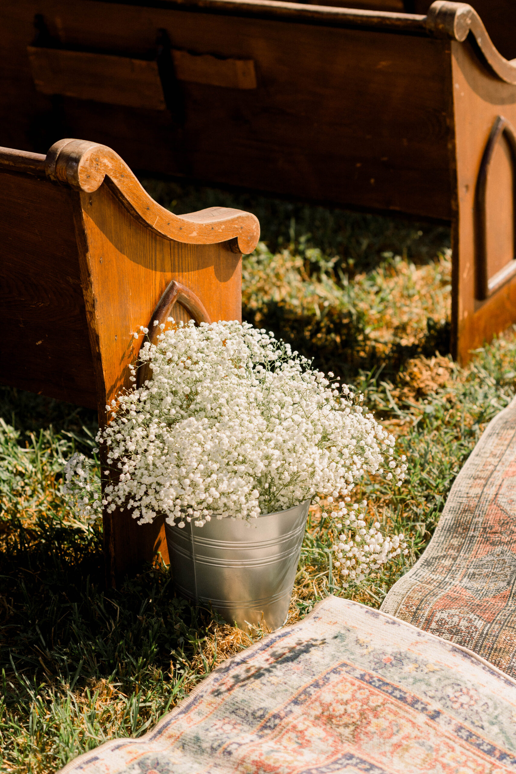 Vintage wood church pew with a floral accent beside a layered wedding aisle rug